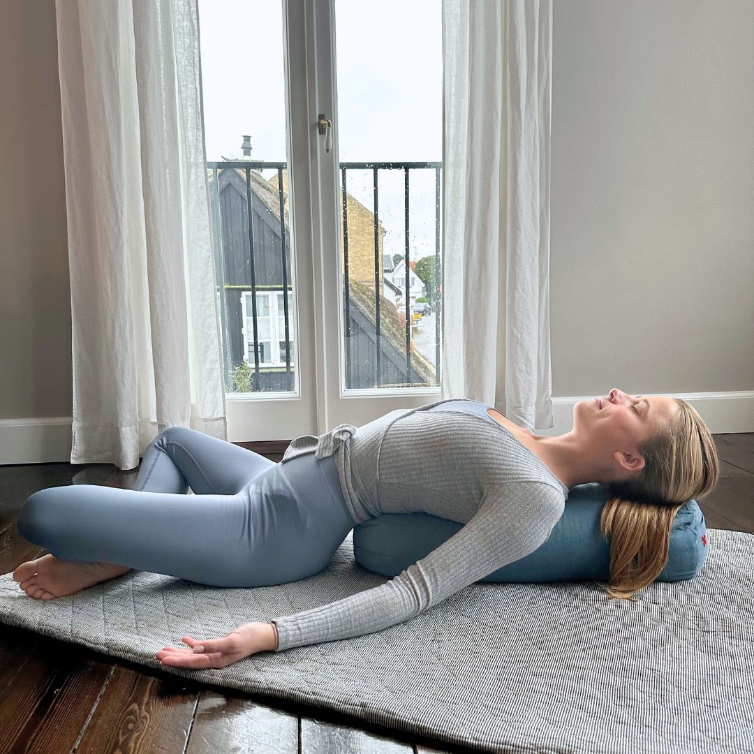 Pige ligger på gulvet oven på yoga bolster i havblå